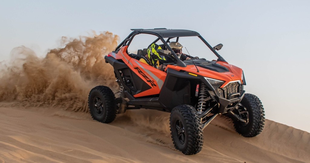 Off-road vehicle speeding on sand dune, kicking up dust.