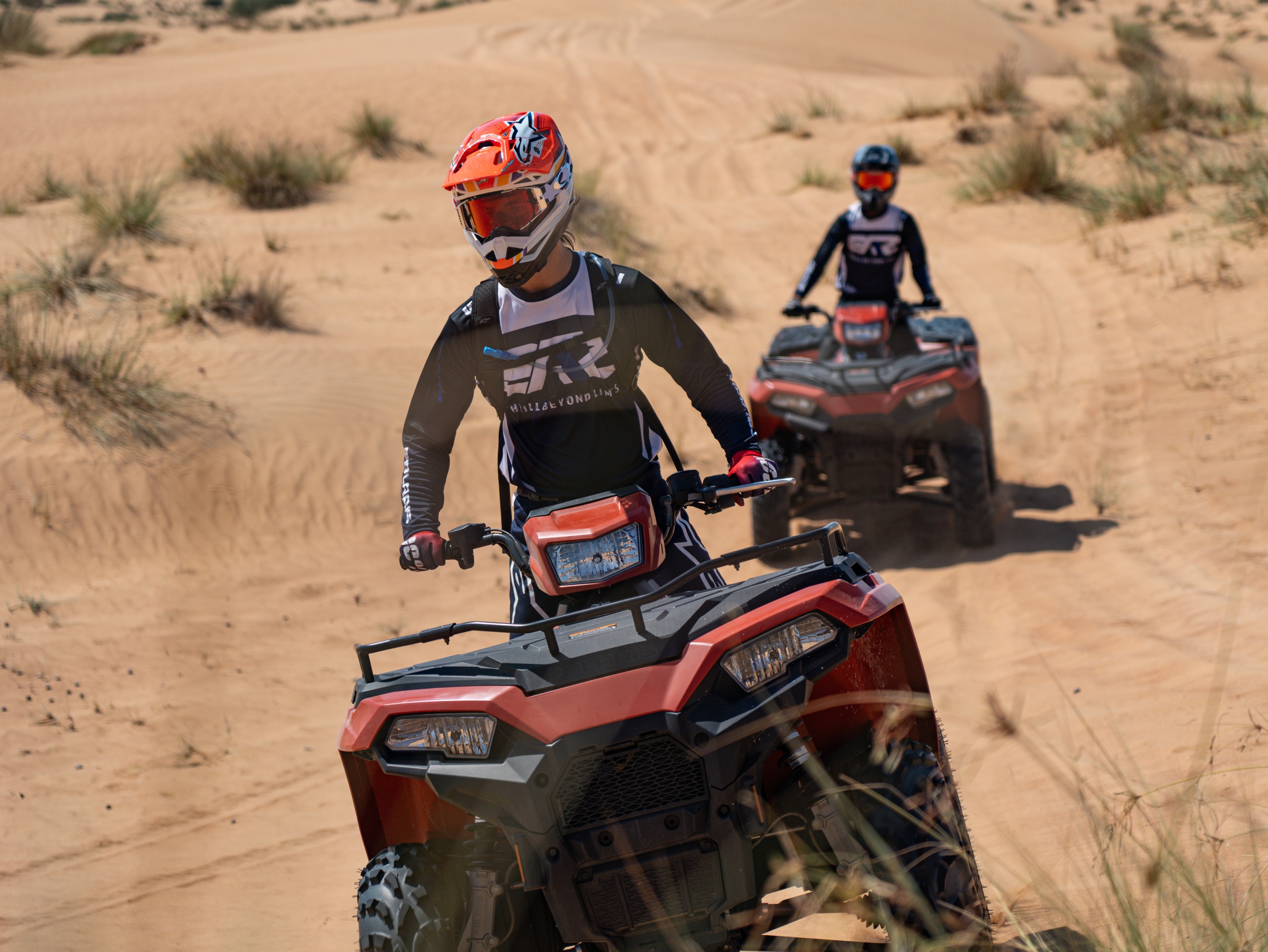 Two people riding ATVs on a sandy desert terrain.
