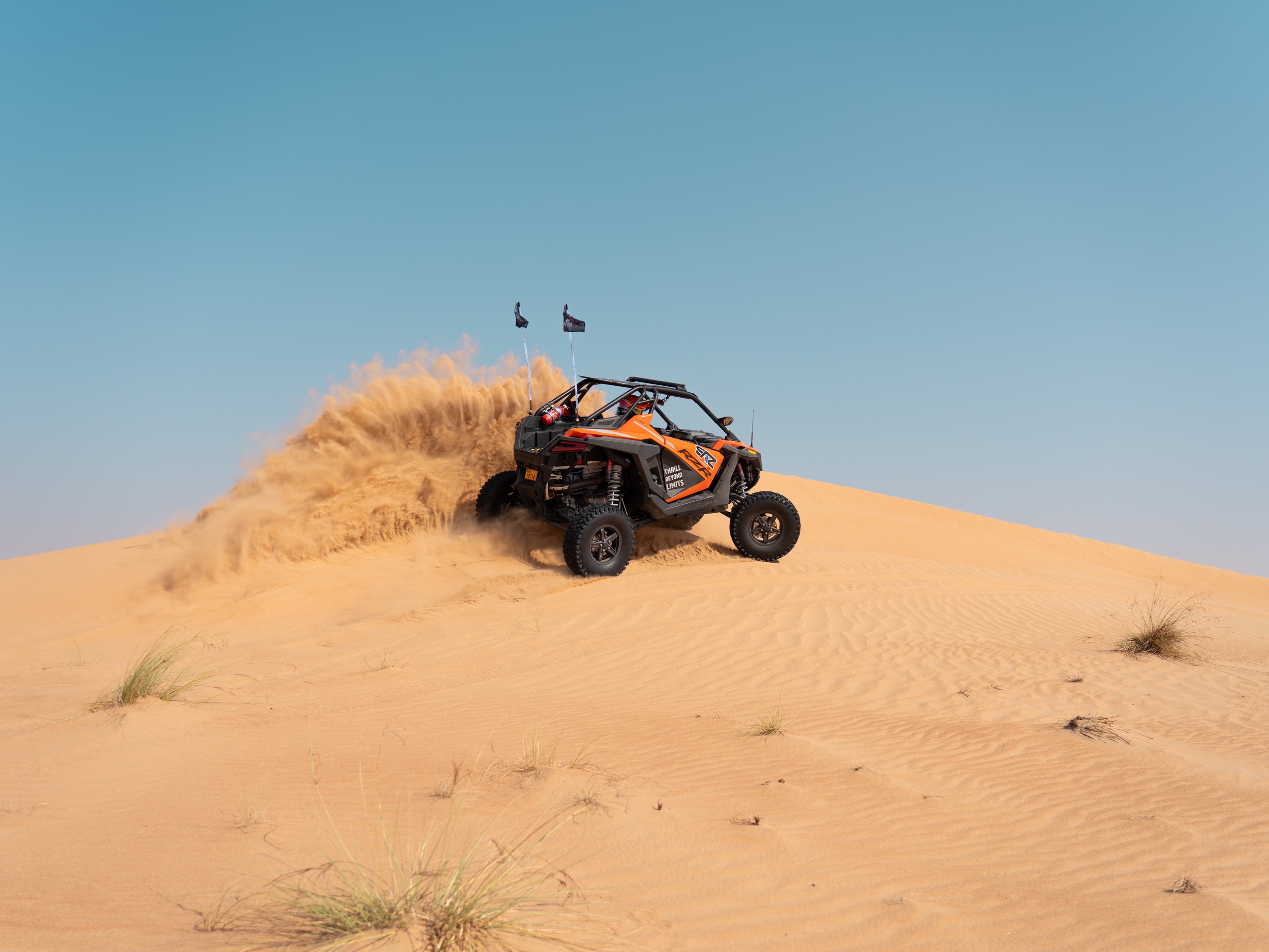 Off-road vehicle driving up a sand dune in the desert.