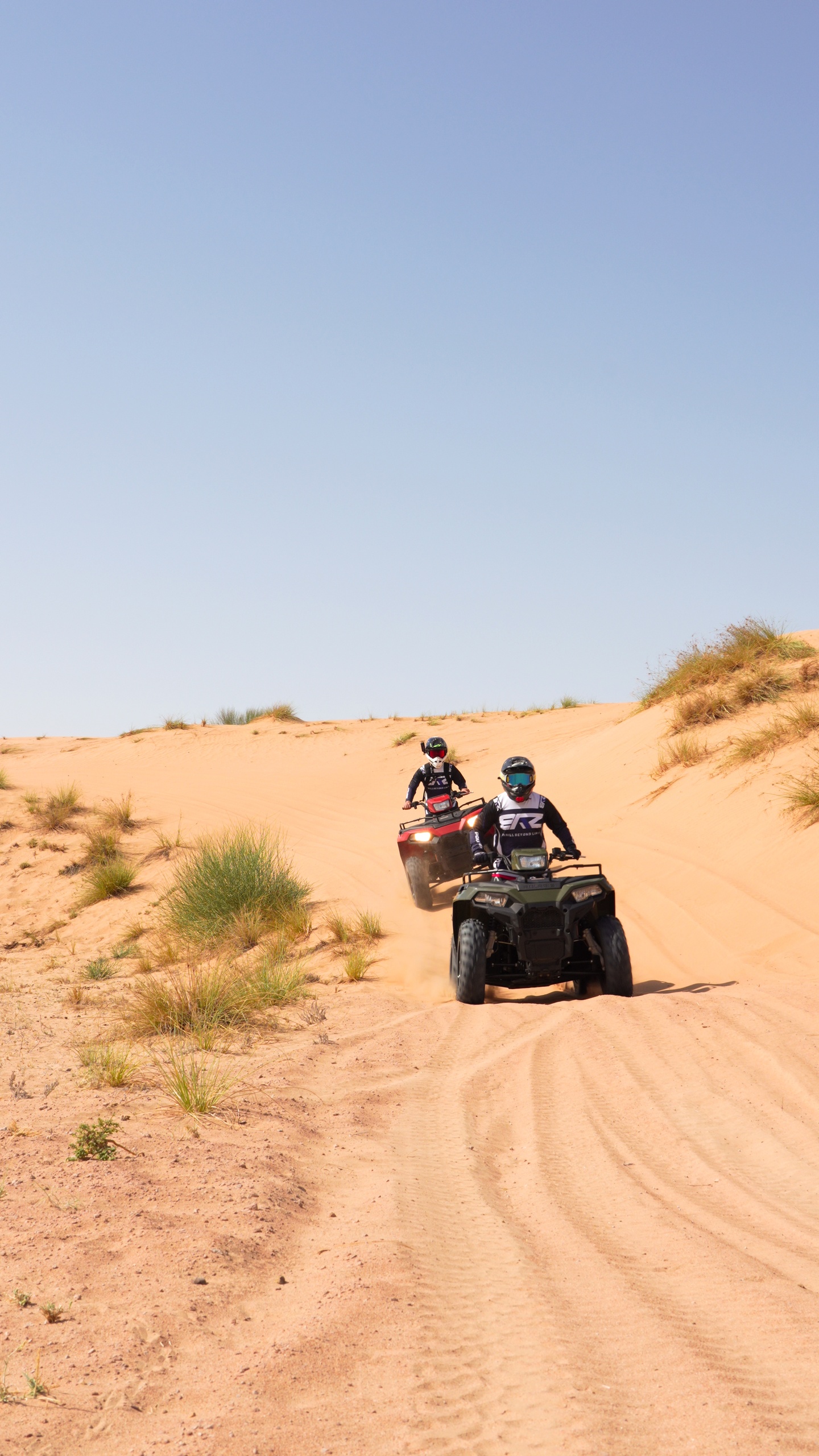 Two people riding ATVs on a sandy desert trail.