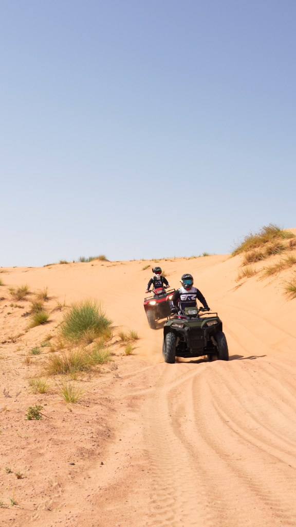 Two people riding ATVs on a sandy desert trail.