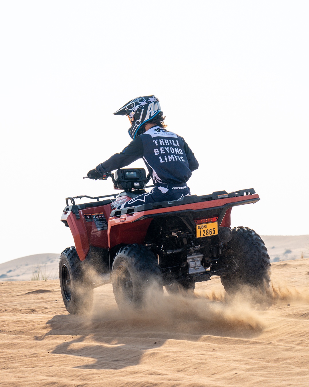 Person riding an ATV on sandy terrain under a clear sky.
