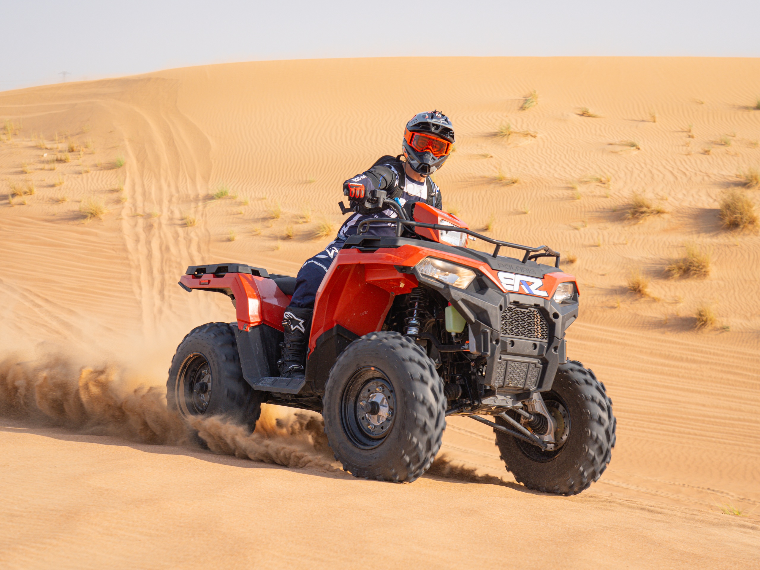 Person riding a red ATV on a sandy desert dune.