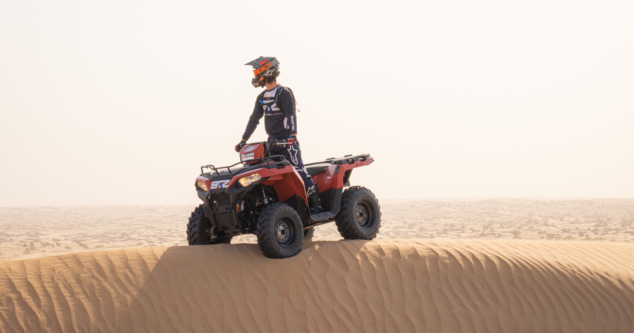 Person on red ATV standing on sandy desert ridge.