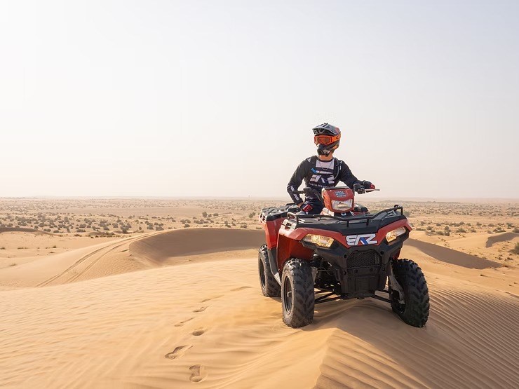Person on a red ATV riding over sand dunes in a desert landscape.