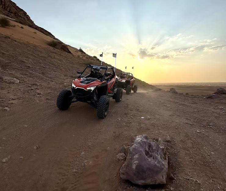 Two off-road vehicles driving on a dirt path at sunset.