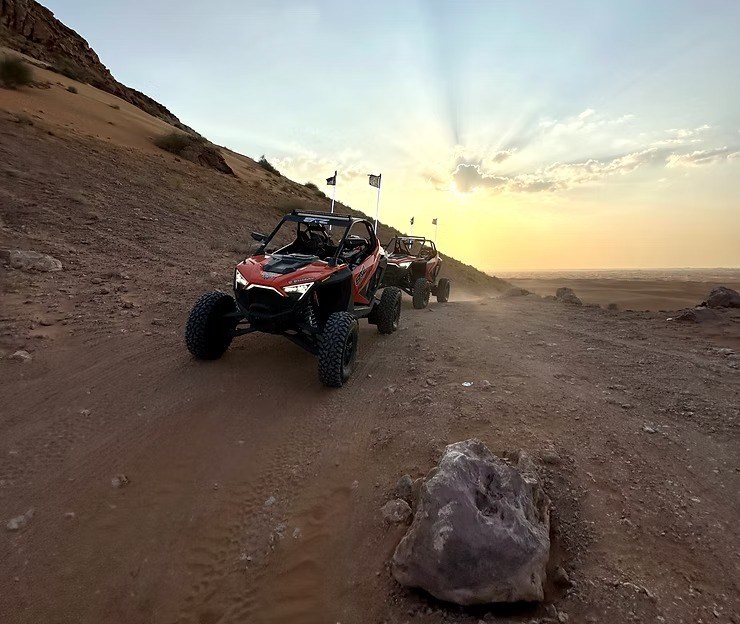 Two off-road vehicles driving on a dirt path at sunset.