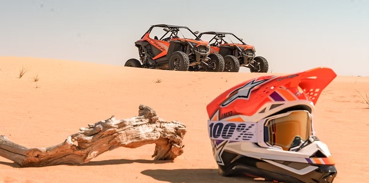 Two off-road vehicles on sand dune, helmet in foreground.