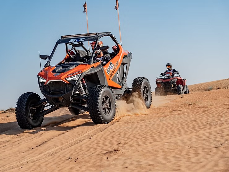 Two off-road vehicles driving on desert sand dunes.