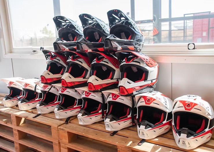 Rows of motocross helmets stacked on wooden pallets by a window.