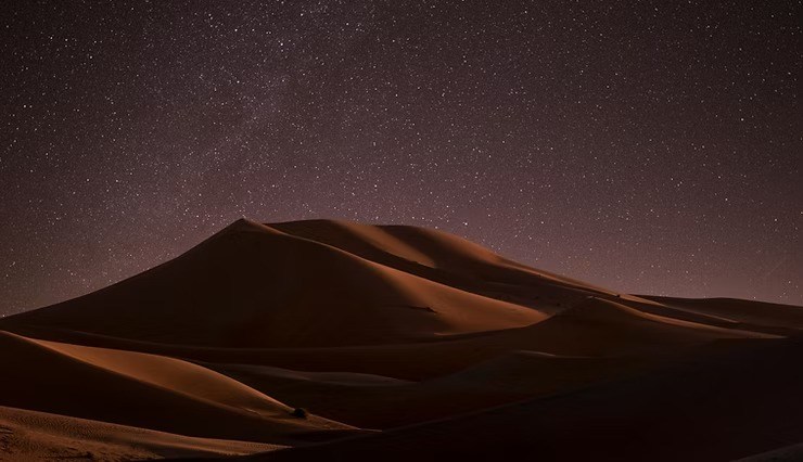 Starry night sky above desert sand dunes.