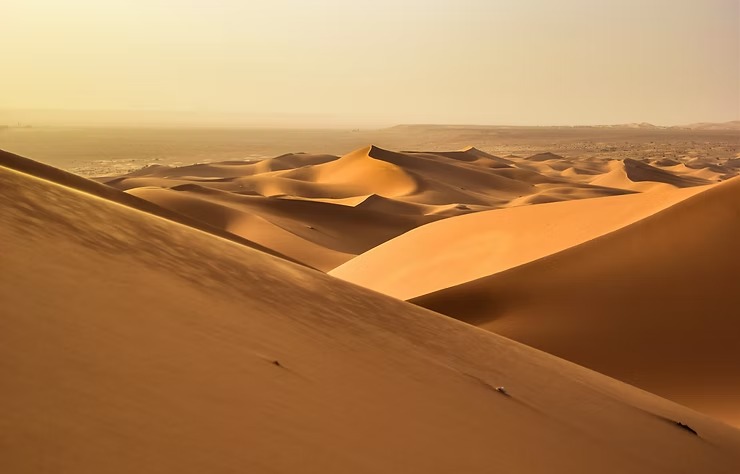 Golden sand dunes under a hazy sky, stretching into the distance.