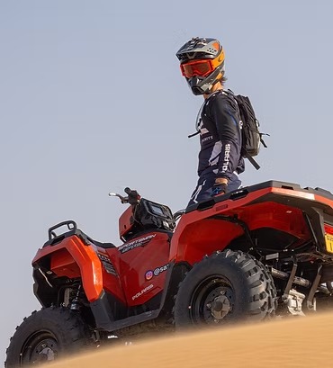 Person in gear on red ATV atop a sand dune.