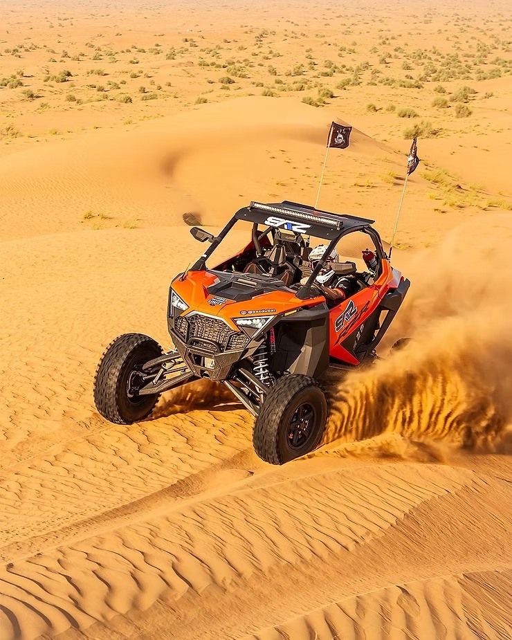 Orange off-road vehicle driving on desert sand dunes.