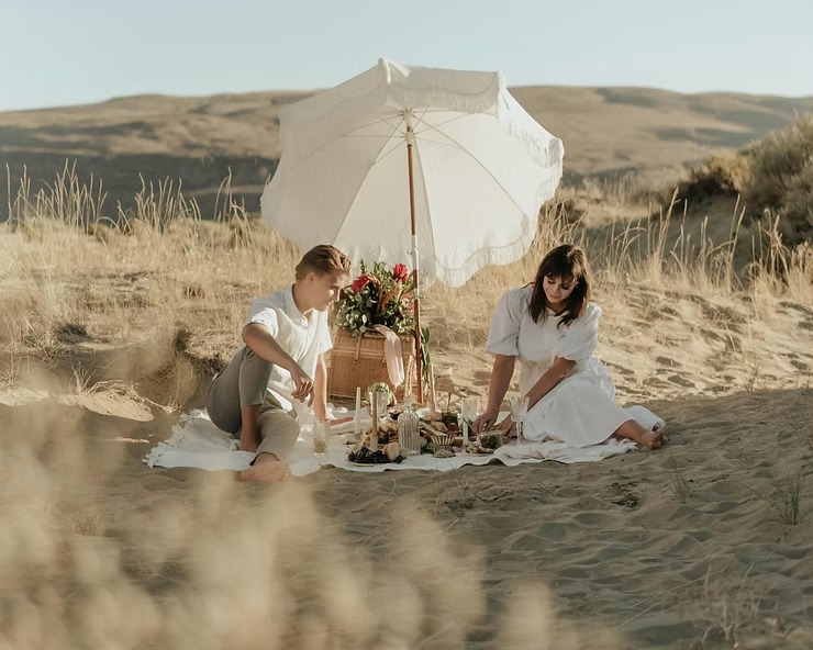 Couple having picnic under a white umbrella in a sandy desert landscape.