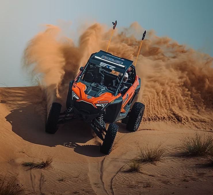 Off-road vehicle kicking up sand in desert terrain.