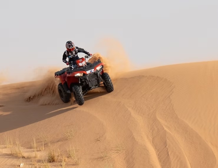 Person riding a red ATV on sand dunes in the desert.