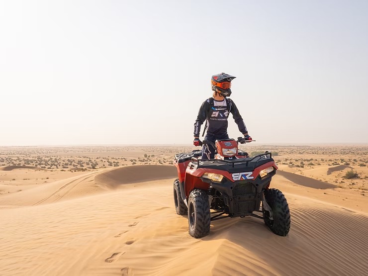 Person on ATV riding through desert dunes.