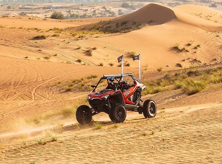Red off-road buggy driving across sandy desert dunes.