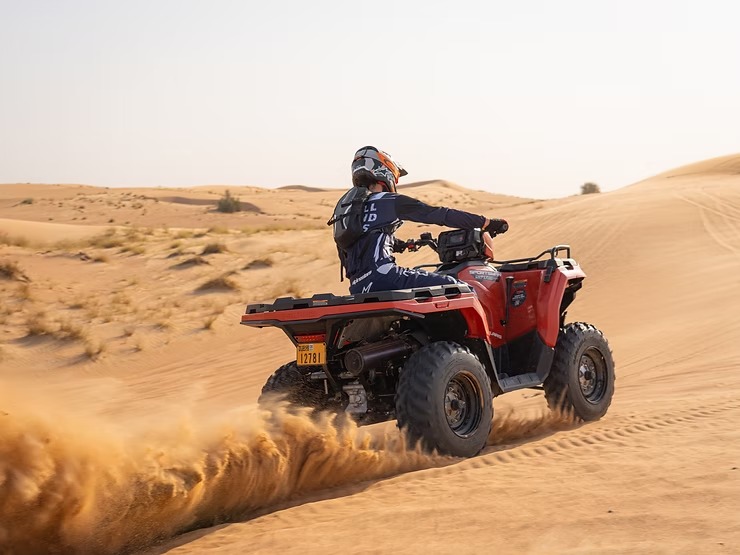 Person riding a red ATV through sandy desert dunes.