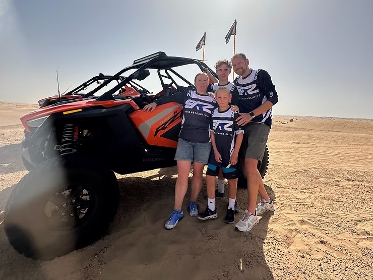 Four people stand by an off-road vehicle in a desert landscape.